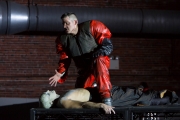 (Top-Bottom): David McFerrin as The Officer threatens Yury Yanowsky as the Man in Boston Lyric Opera’s new “Opera Annex” production of Philip Glass’s dystopian “In the Penal Colony” based on the Franz Kafka short story, and in a limited run Nov 11-15 at the historic Cyclorama at the Boston Center for the Arts.